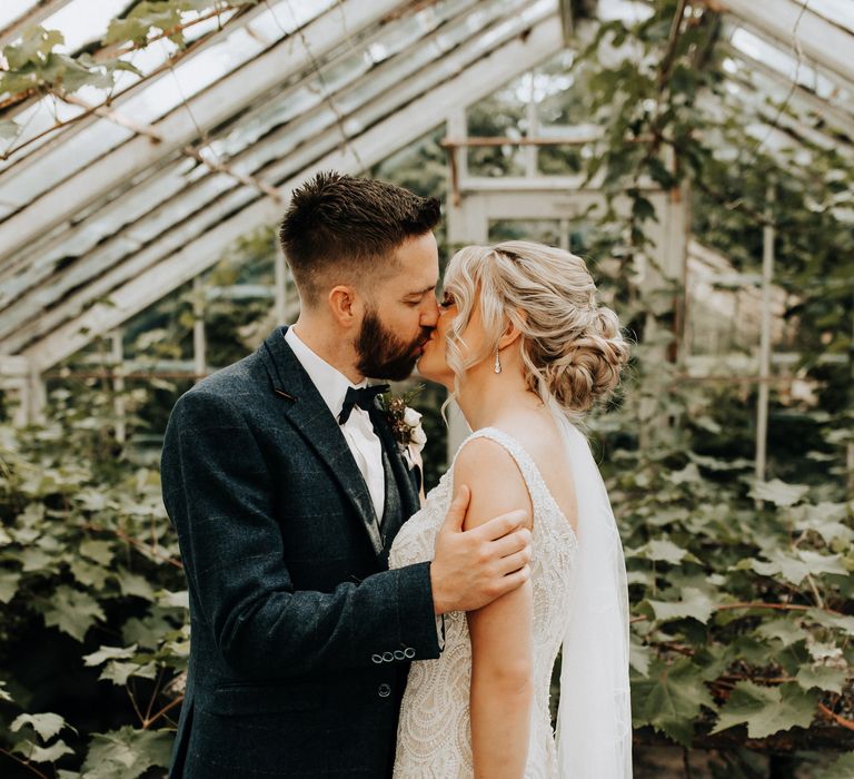 Bride and groom share a kiss in greenhouse 