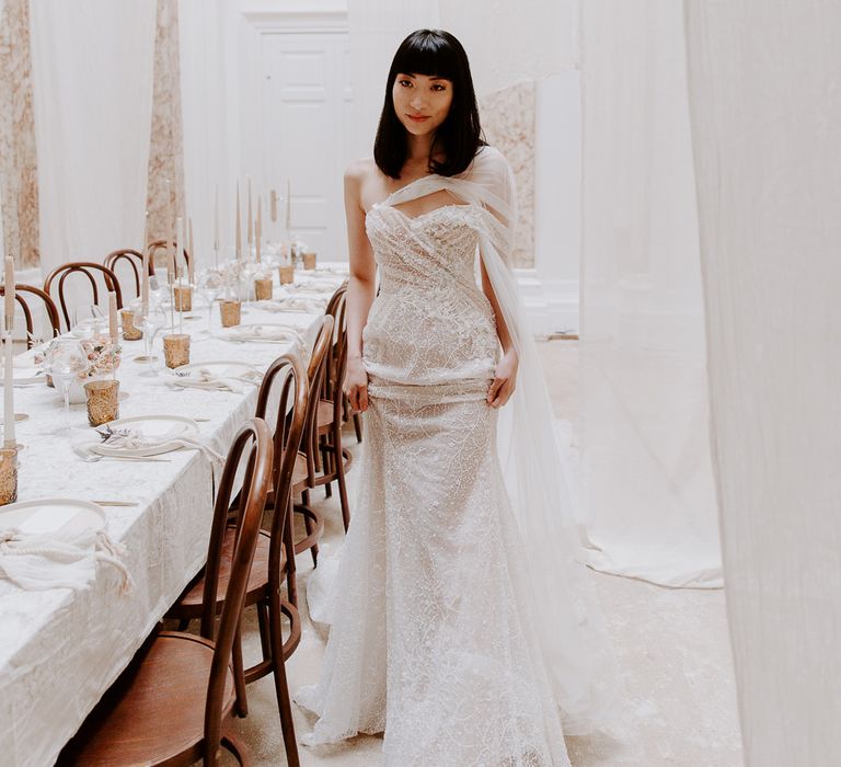 South Asian bride with shoulder length hair and a fringe in a lace strapless wedding dress standing in the minimal reception at Bylaugh Hall 