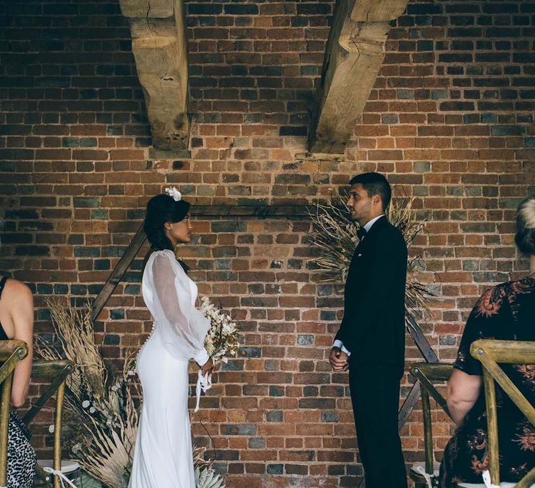 Bride in a fitted wedding dress and groom in a tuxedo at their boho black tie wedding ceremony at Brickhouse Vineyard with hexagonal altar and dried flower arrangements 