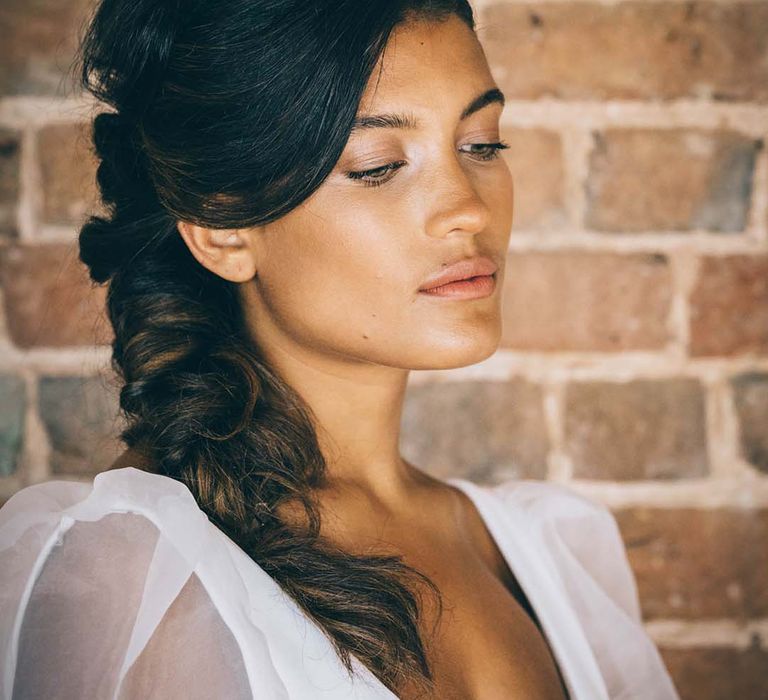 Beautiful bride with natural wedding makeup and a side braided up do wearing a white flower headband 