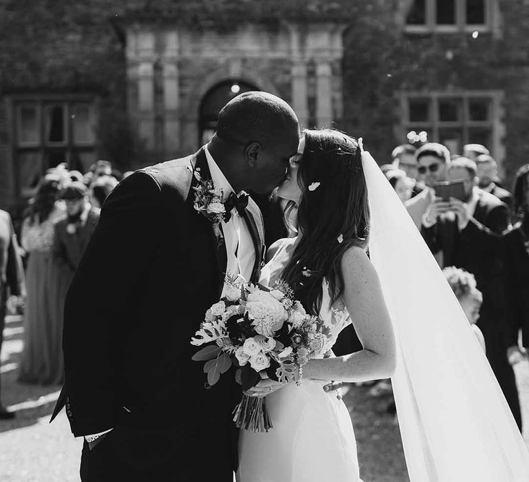 Bride & Groom kiss with confetti falling on them as guests celebrate at Cefn Tilla Court wedding