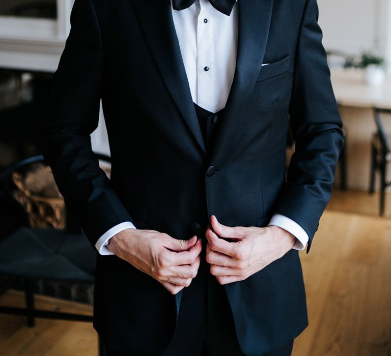 Groom does up the buttons on his black tie blazer