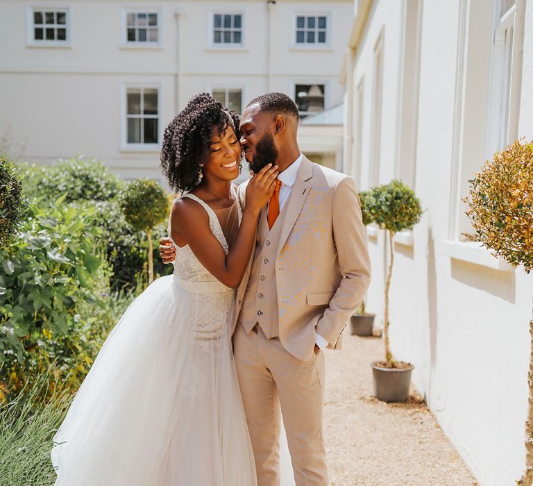 Groom in a beige three-piece suit kissing his bride in the courtyard at Modern Hall, London in a plunging neckline wedding dress by Ersa Atelier