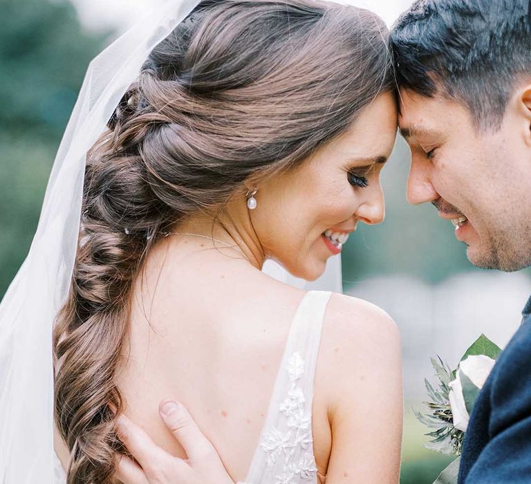 Groom in blue wool jacket touching his brides back with a low V and long curled hair 