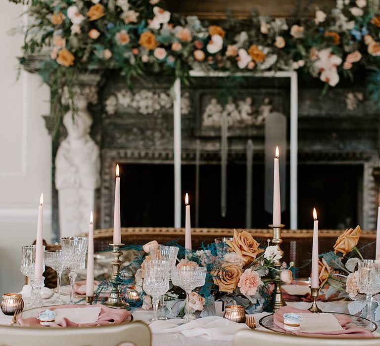 Elegant wedding table decor with pink taper candles, gold candlesticks, cut glass goblets, and cafe au late floral arrangements 