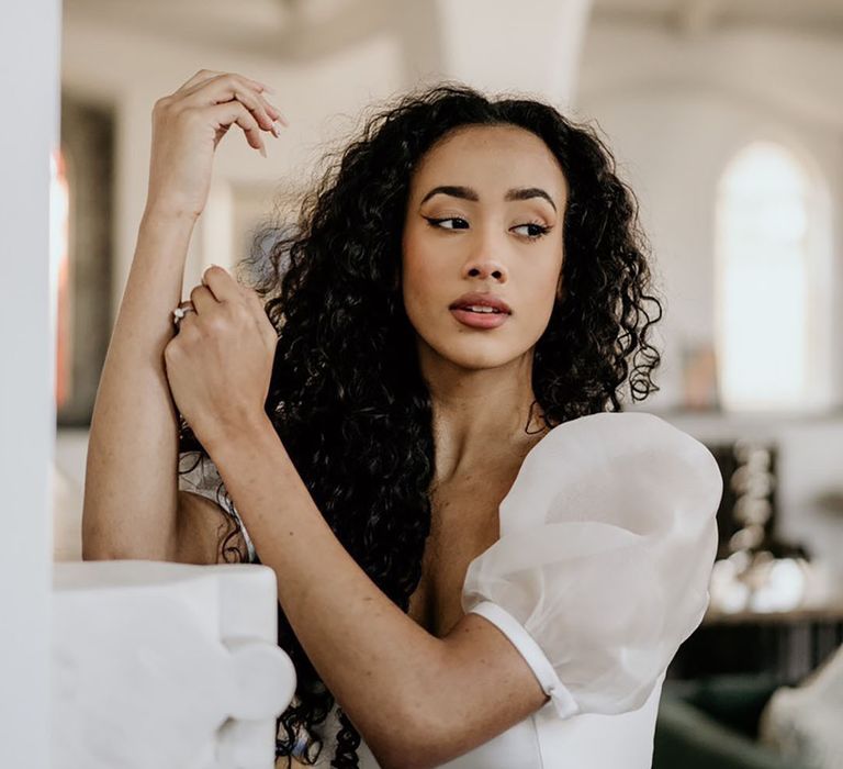 Black bride with naturally curly hair and makeup wearing a Story Of My Dress bridal gown with sheer sleeves 