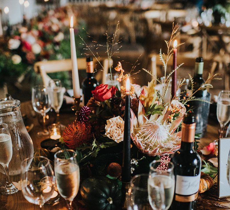 autumn theme wedding centrepiece flowers with king protea, roses and carnations surrounded by taper candles 