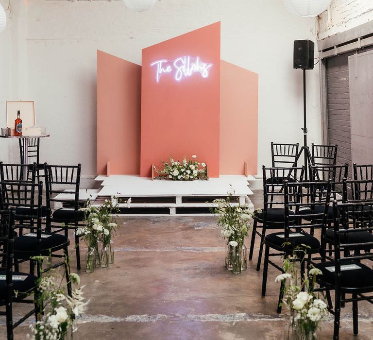 Wedding altar style with pink background and white neon sign with the couple's new last names, white hanging paper lanterns and white flower decor