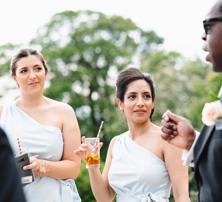 Groom in suit wearing sunglasses socialises with the bridesmaids in pastel blue dresses