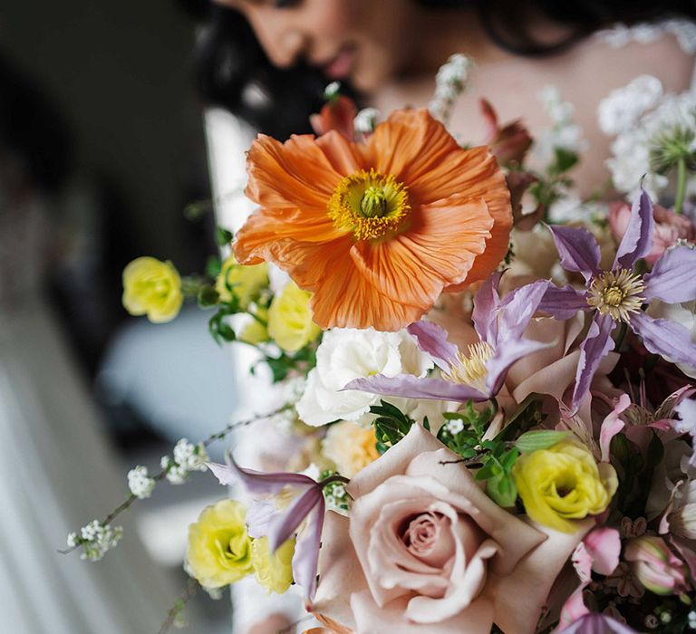 Bride holding bright and colourful wedding bouquet with orange, pink, purple, yellow and white flowers including poppies and roses