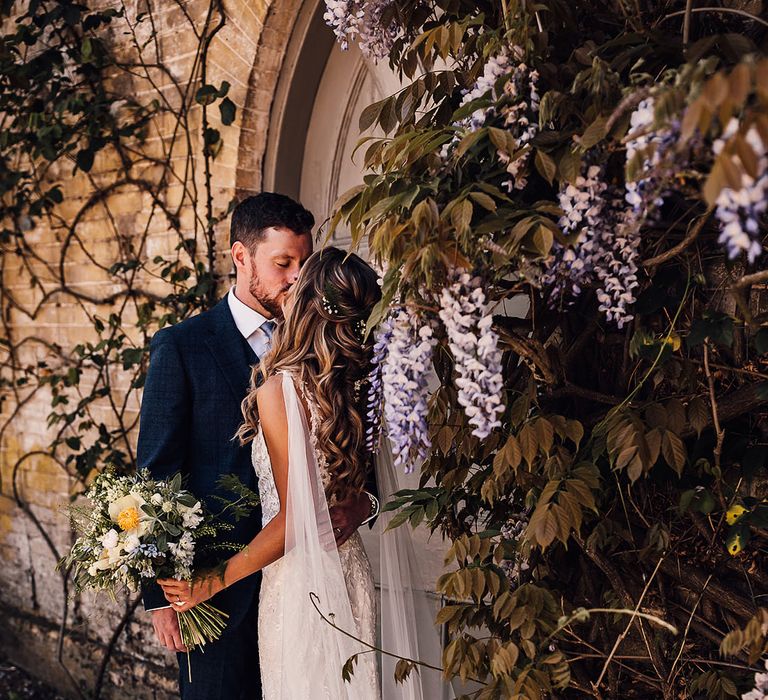 Bride in lace wedding dress with detachable tulle wings and groom in blue three piece suit kiss 