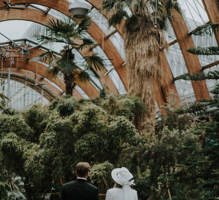 Bride in white wedding trouser suit holding hands and walking with groom in black tie