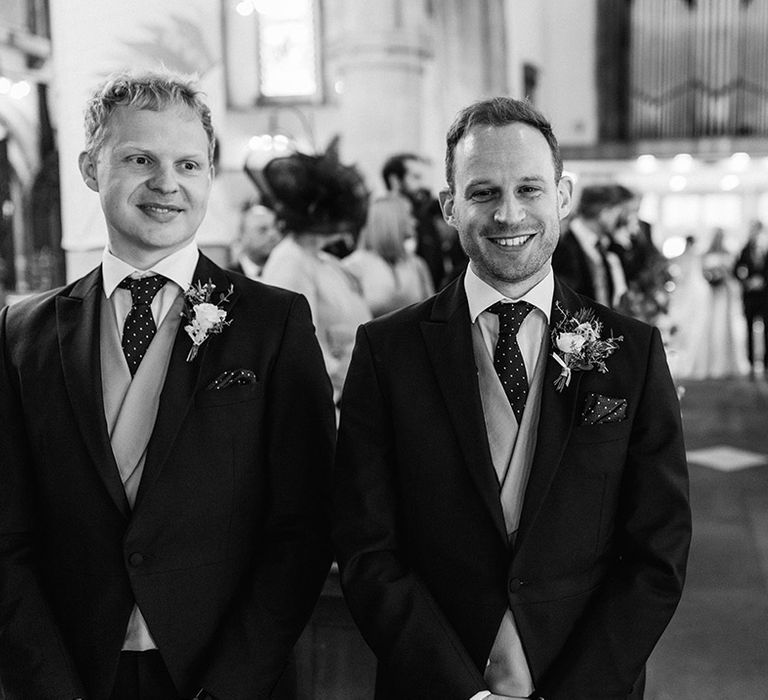 Groom smiles at the camera with his best man standing next to him in matching suits 