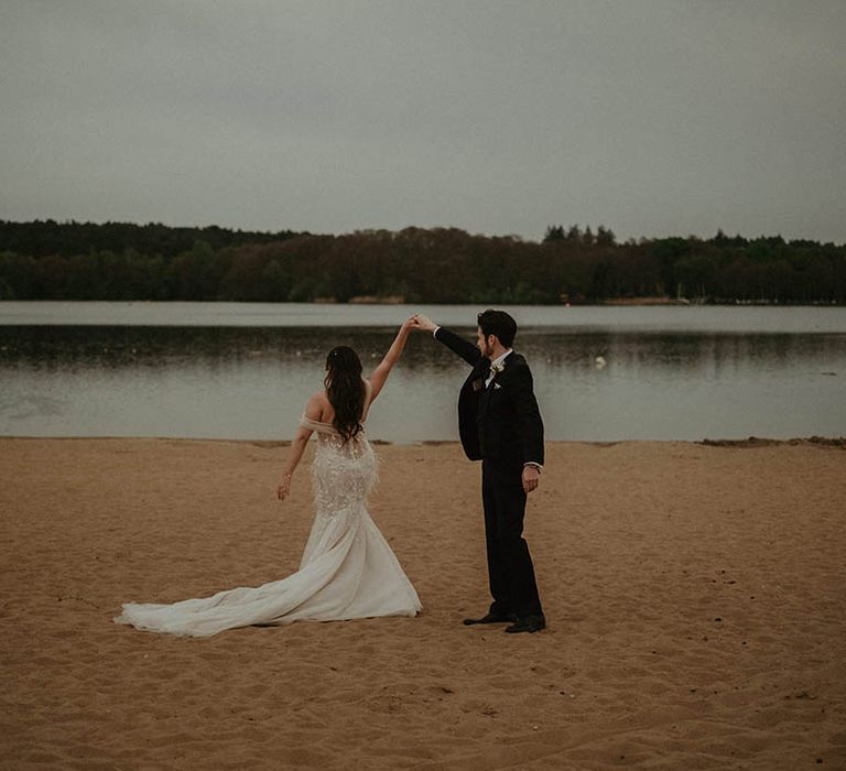 Groom in blue suit twirls the bride in a sparkly feather tulle wedding dress around on the beach