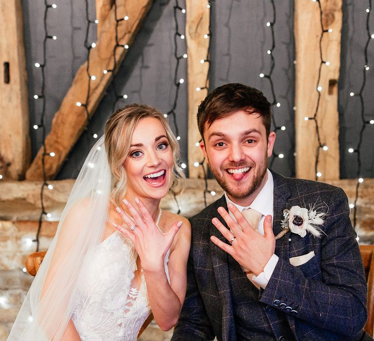 Bride and groom sit to sign the register and both show off their new wedding bands to the camera 