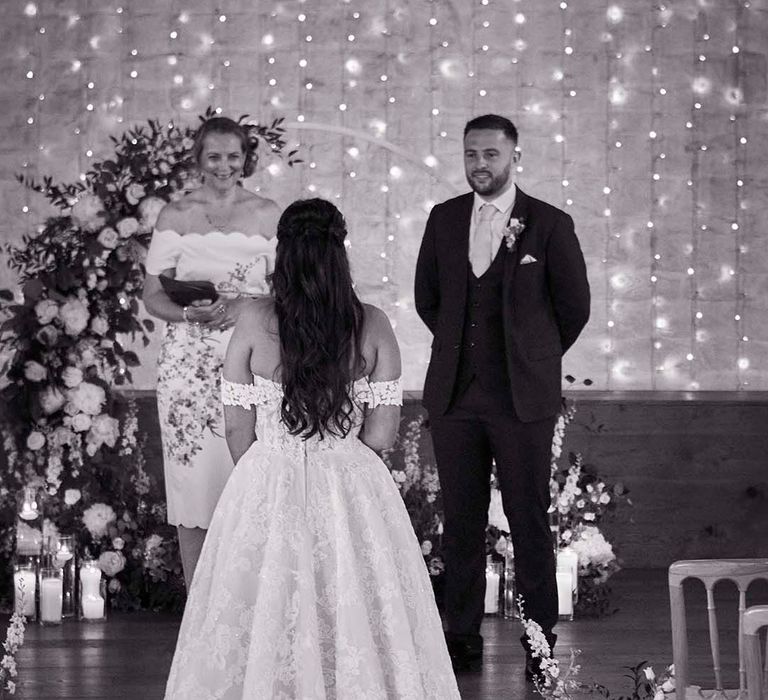 rustic barn wedding ceremony entrance with fairy light backdrop and bride in an of the shoulder lace wedding dress