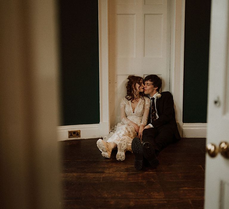 Bride & groom sit in front of door on the floor for moody and gothic pictures on their wedding day