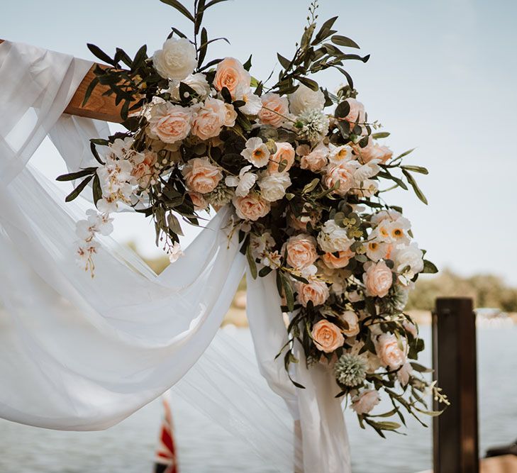 Pastel white and pink florals on wooden arch draped in white fabric 