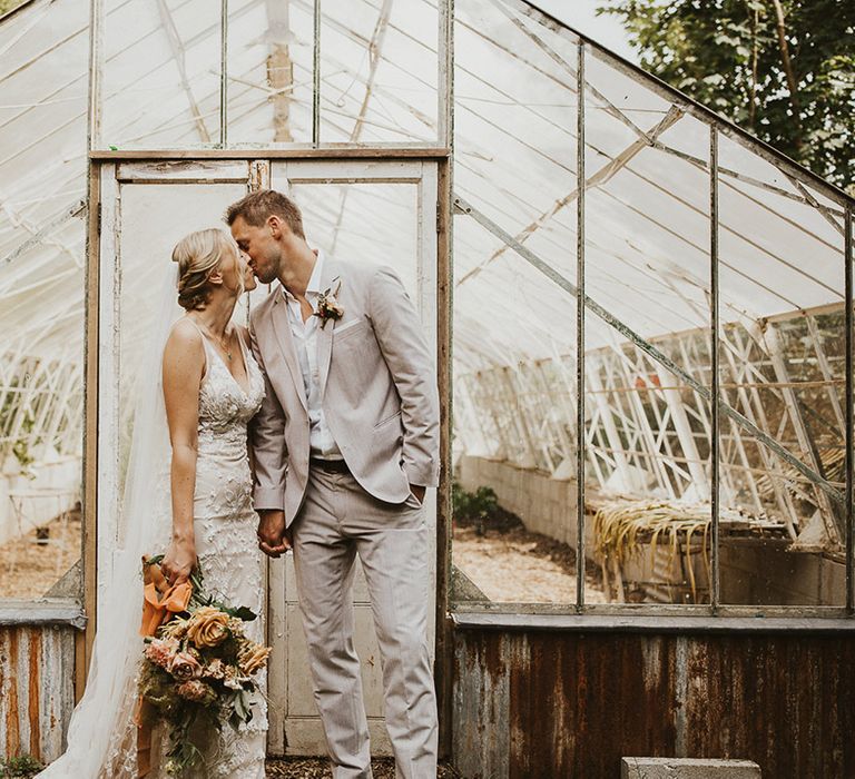 The bride and groom share a kiss in front of the greenhouse at Nancarrow Farm wedding venue 