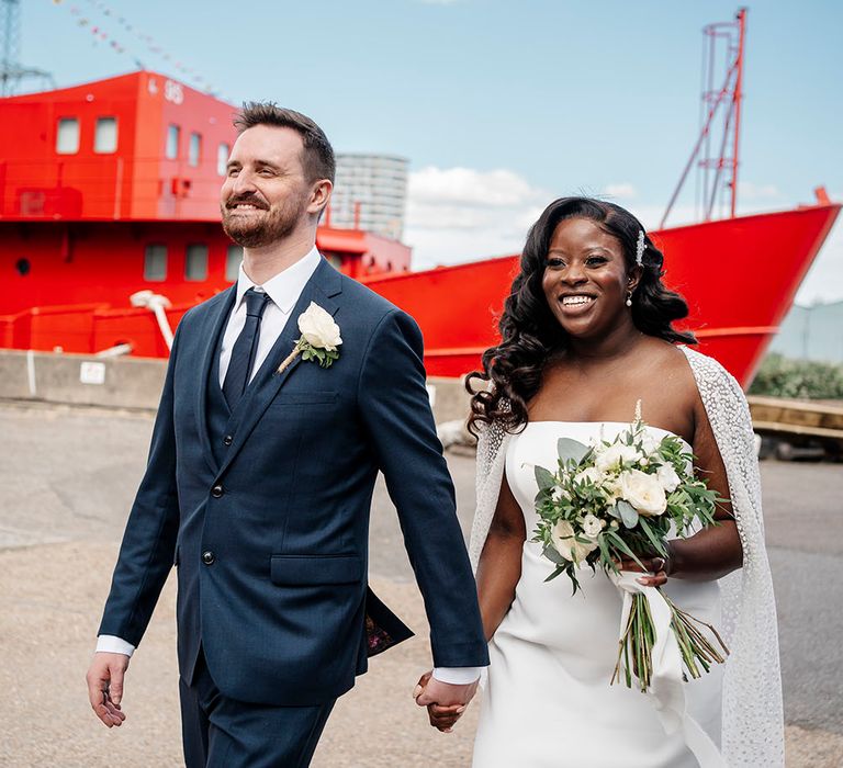 Bride holds white bridal bouquet complete with green foliage as groom wears matching buttonhole 