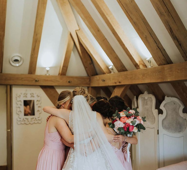 Bride in a floral lace wedding dress has a group hug with her bride tribe in pink dresses before the wedding 