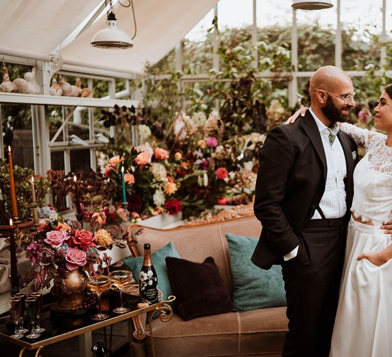 Bride in three quarter length sleeve bridal separates with lace detailing and full satin skirt embracing groom in black tuxedo with hand-painted silk cravat and handkerchief 