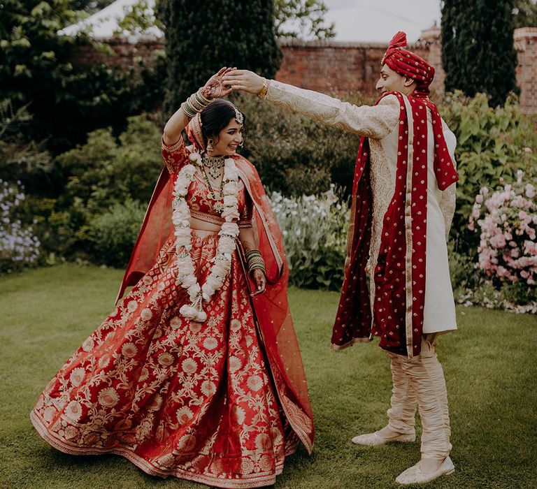 Groom in red and white sherwani spins his bride who wears red and gold lehenga 