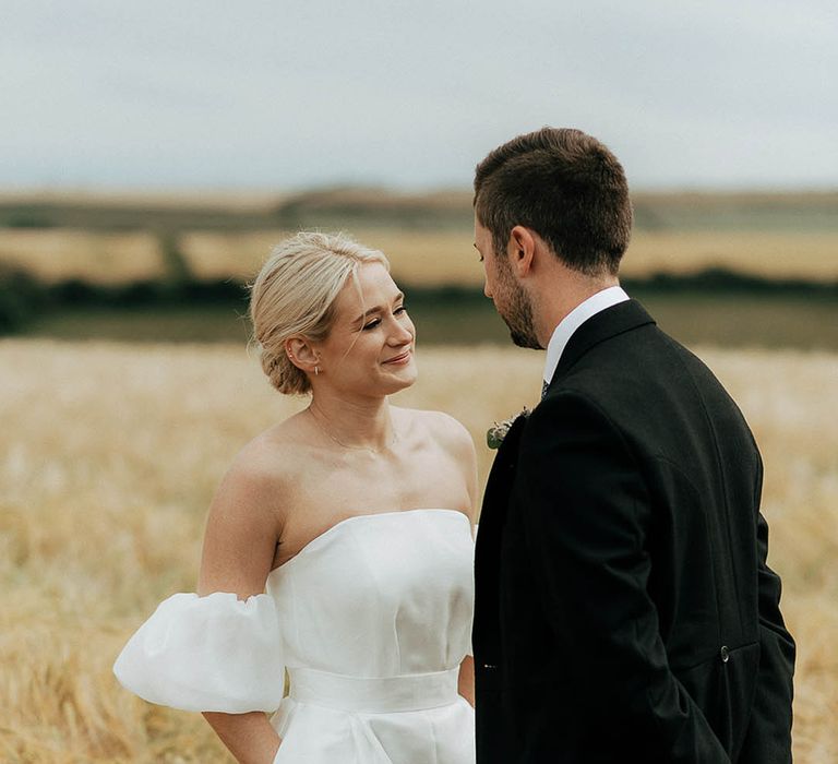 Bride wears Jesus Peiro wedding dress and places her hand in the pockets as she stands in golden fields with her groom