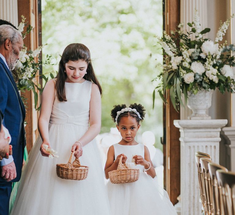 Flower girls in white dresses and tutu styled skirts walk down the aisle with wicker baskets 