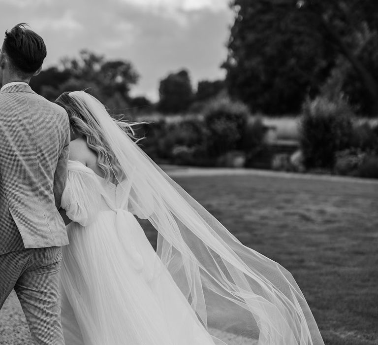 Bride in whimsical wedding dress with tulle skirt and long wedding veil walking along with the groom