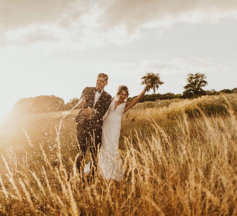 The groom pops champagne to celebrate the wedding during golden hour 