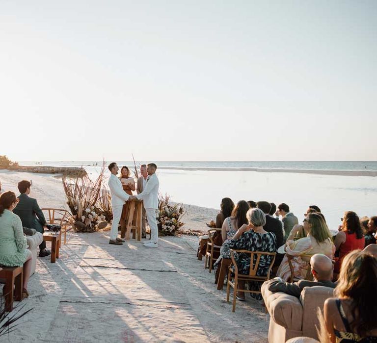 Grooms in complimenting white wedding suits at the alter on white sand beach wedding in Mexico 