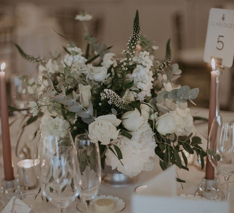 Neutral taper candles with white flower table centrepiece with table number sign 