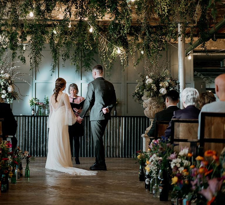 Heartfelt wedding ceremony between pregnant bride and groom wearing a grey suit at industrial wedding with wildflower wedding theme 