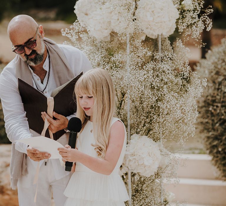 little girl in a white dress performing a wedding reading at outdoor wedding ceremony in ibiza