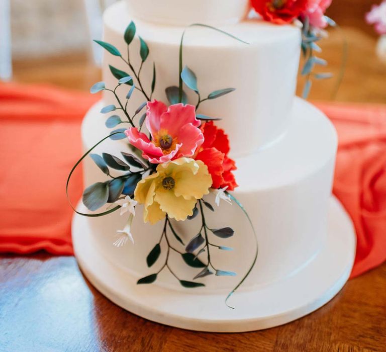 Misshapen three tiered wedding cake with white icing and seasonal flower and foliage cake toppers 