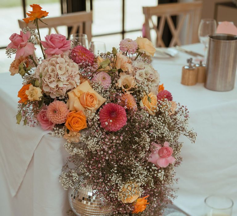 Pink and orange wedding flower decorations with gypsophila, roses, dahlias and more with disco balls 