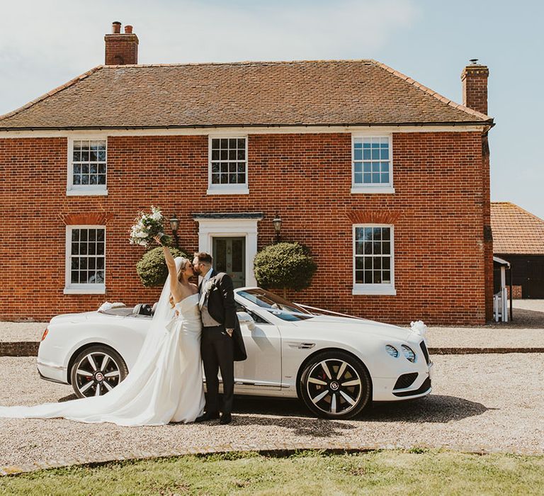 The bride and groom pose next to their white convertible sports car wedding transport 