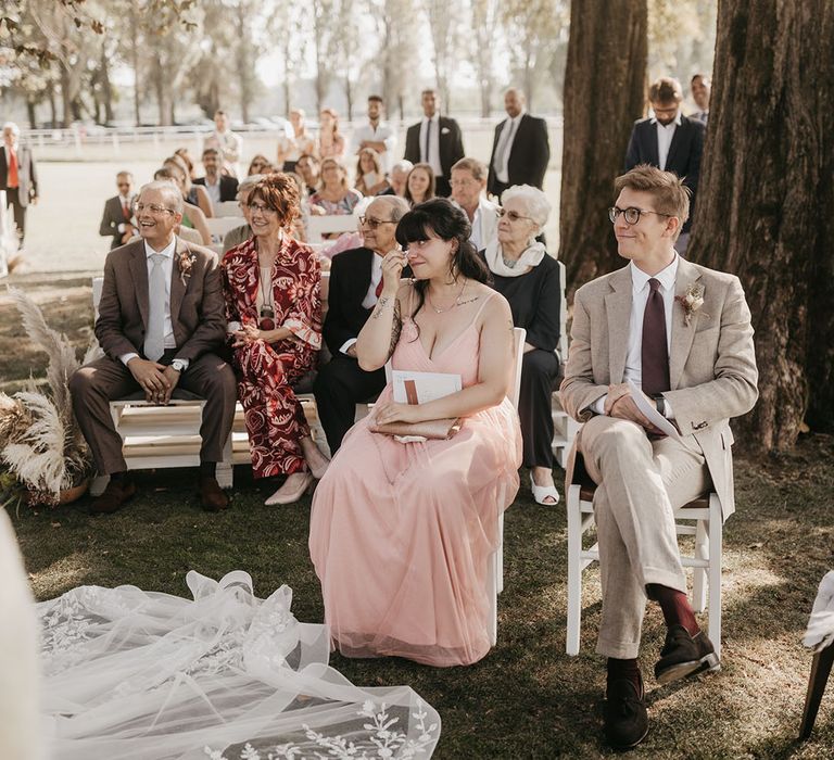 emotional wedding guests in a pink dress wiping away tears at the outdoor wedding ceremony 