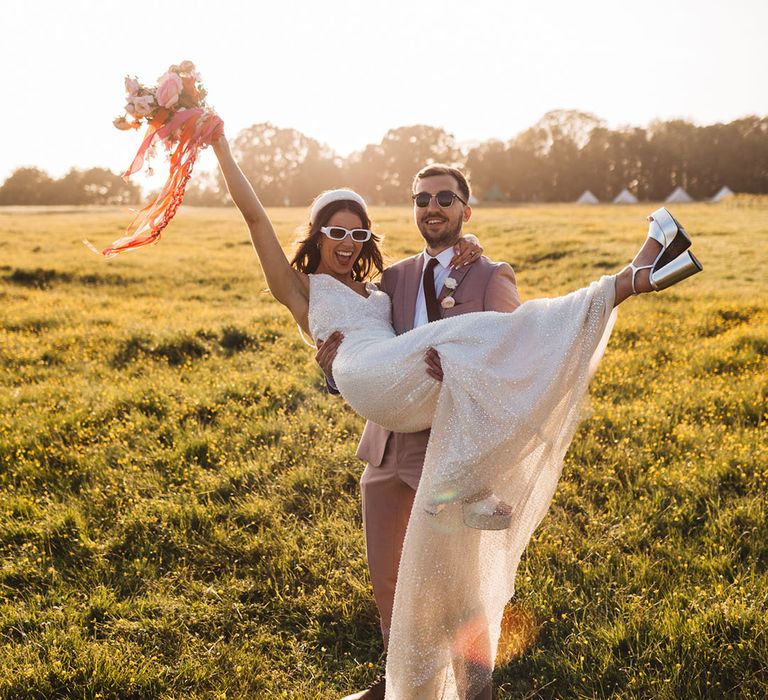 Groom in pink taupe suit lifting bride in sparkly wedding dress with chunky silver platform shoes 