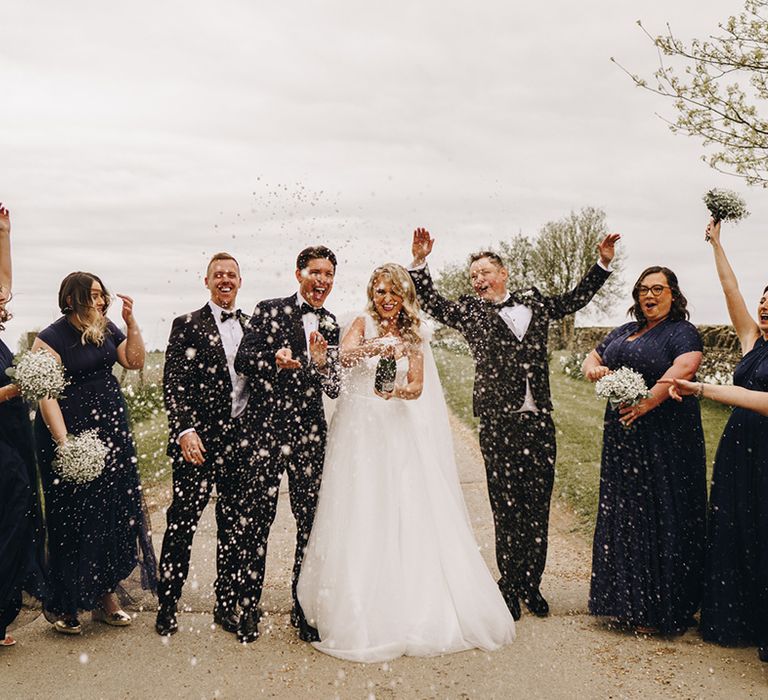 Champagne pop moment with groomsmen in black tie and bridesmaids in navy bridesmaid dresses 