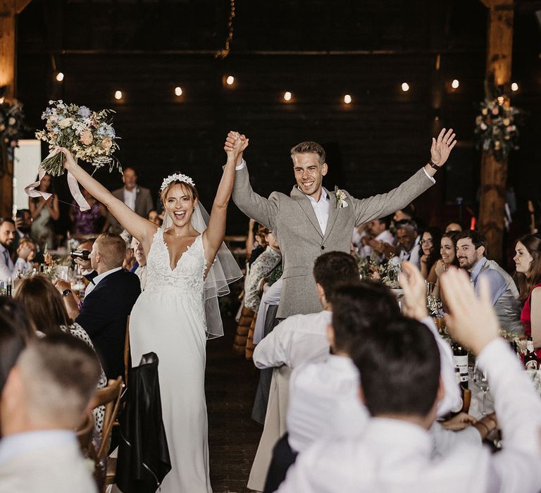 The bride and groom enter their wedding reception with their hands raised in the air 