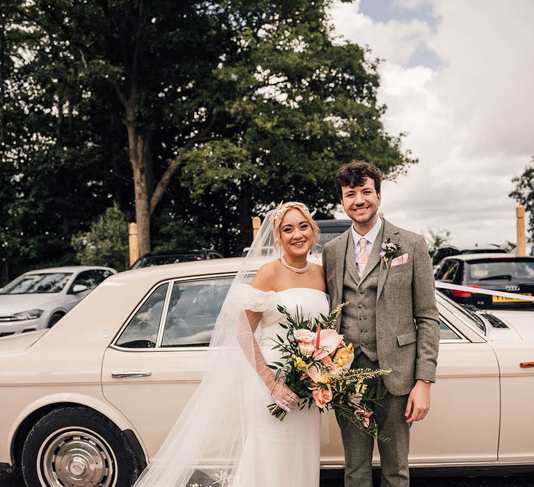 The bride and groom stand next to their wedding car