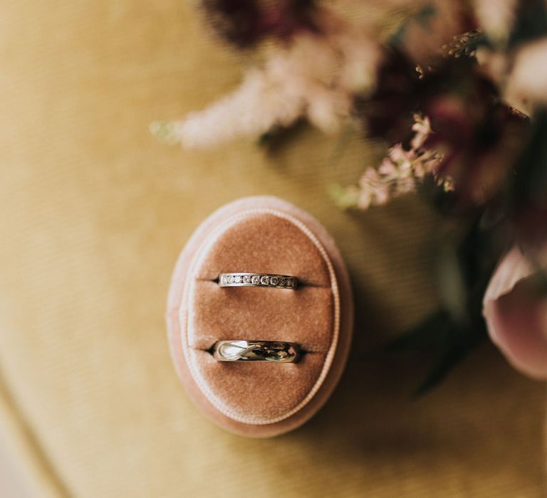 Oval shaped pink velvet ring box with the bride and groom's wedding bands 