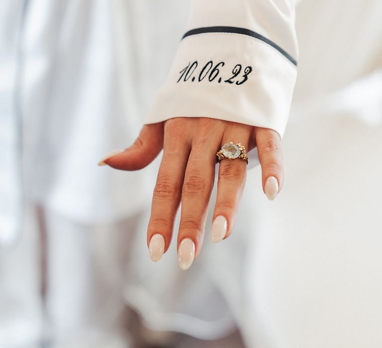 Bride wearing personalised white satin pyjamas with diamond ring and neutral wedding nails 