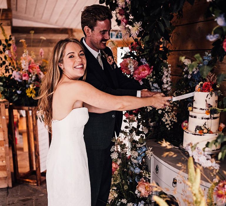 The bride and groom cut their rustic wedding cake with semi-naked icing 