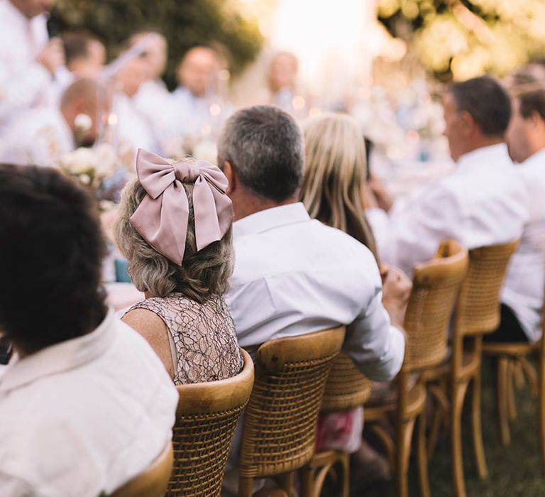 Wedding guests seated at outdoor wedding breakfast with wedding guest wearing hair bow 