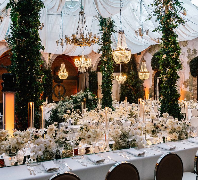 Opulent chandeliers, foliage and cosy lighting with white wedding theme and tablescape 