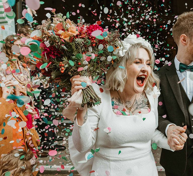 Pastel colourful confetti exit for bride in square neck long sleeve short wedding dress with headband and groom in black suit with green tie 