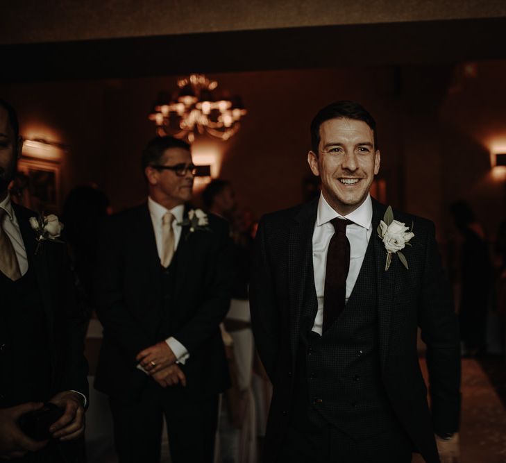 Happy groom waiting for his bride-to-be wearing burgundy tie and while pocket flower for Christmas wedding